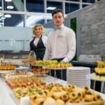 caters of cater4ingg company standing behind a buffet table at a corporate event.